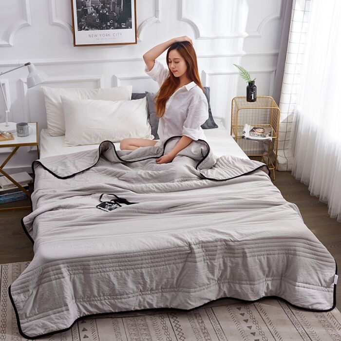 Young woman with her dog sitting on the light grey variant of cooling bed sheets