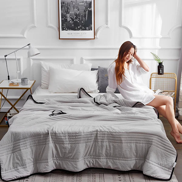 Light grey variant of cooling bed sheets displayed on a bed, with a middle-aged woman sitting comfortably. Experience superior comfort and temperature regulation for a restful night's sleep.